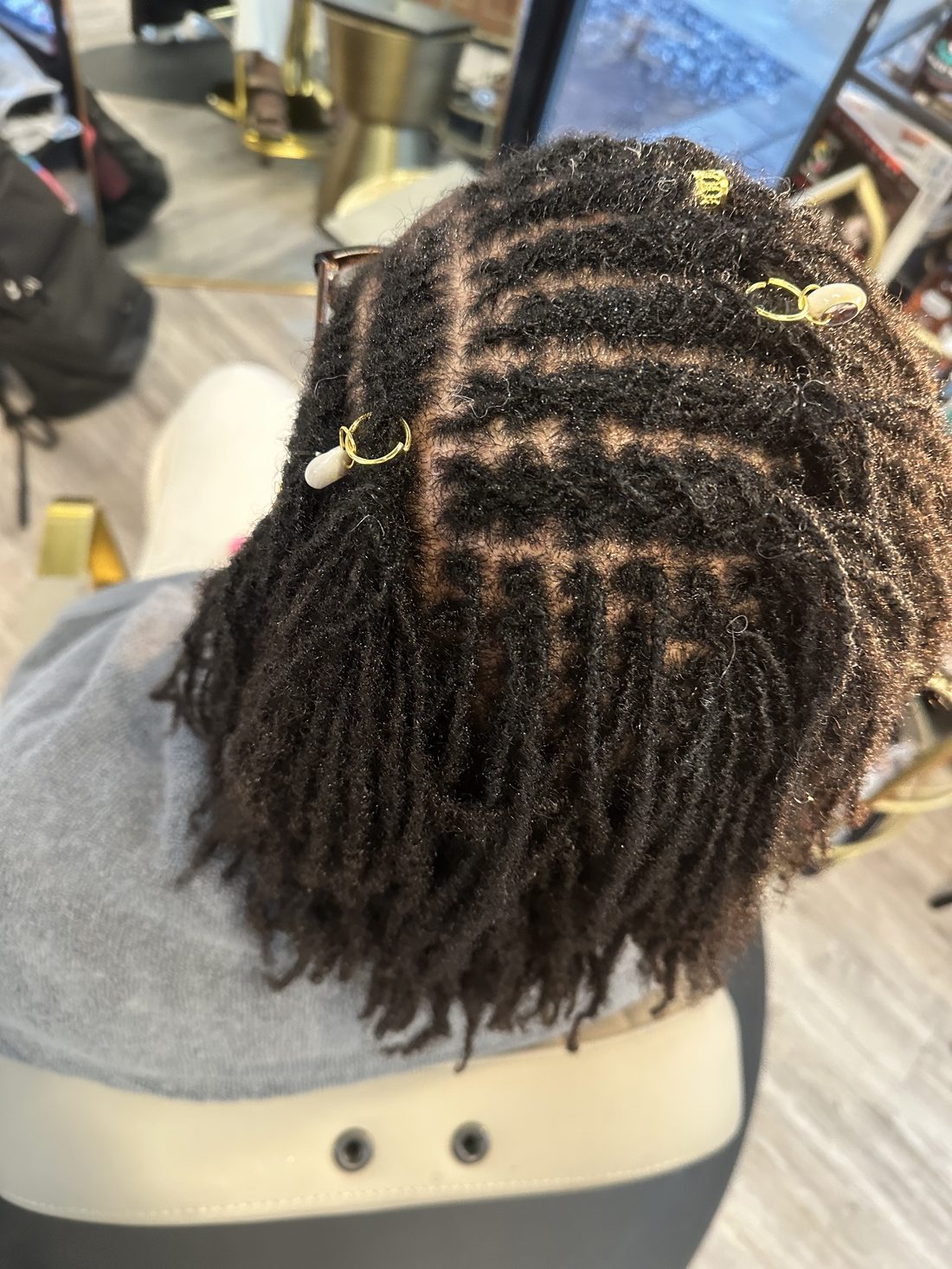 Small locs freshly retwisted in a precise parting grid, finished with gold cuffs