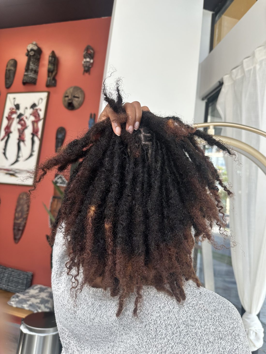 A hand lifting a section of locs to show clean, freshly retwisted roots
