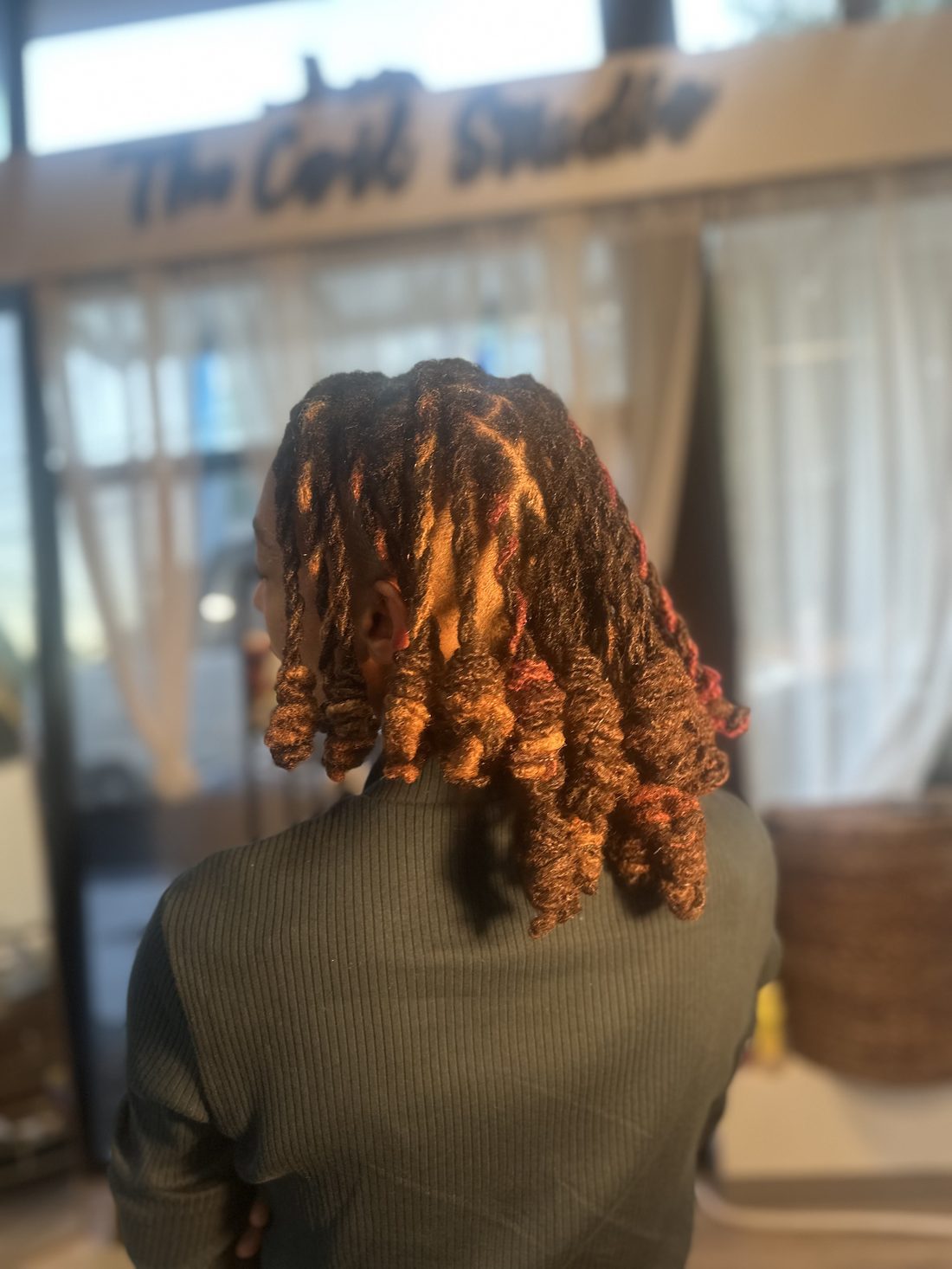 Copper locs set in barrel curls, photographed under The Coil Studio sign